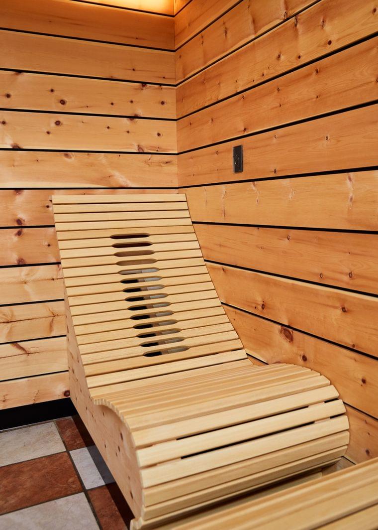 Ergonomic wooden lounger in a modern sauna with wood panel walls